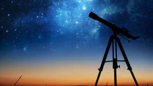telescope silhouette in front of night sky with stars.